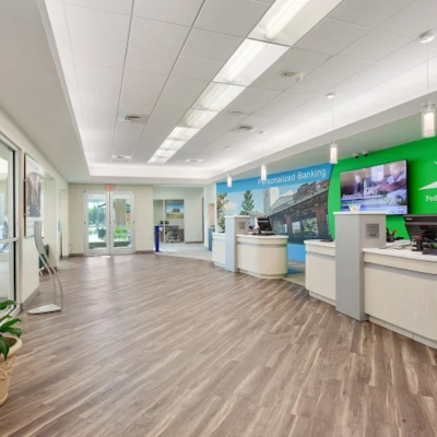 Bank lobby with wood-look flooring, curved counters, colorful mural, and glass entrance doors.